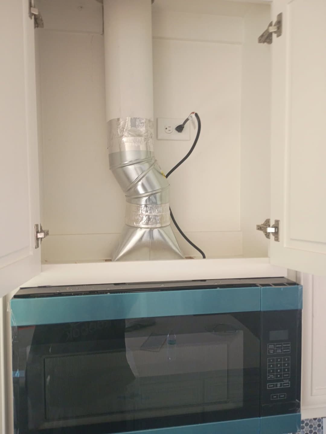 Microwave with installed ductwork and electrical outlet in kitchen cabinet space.