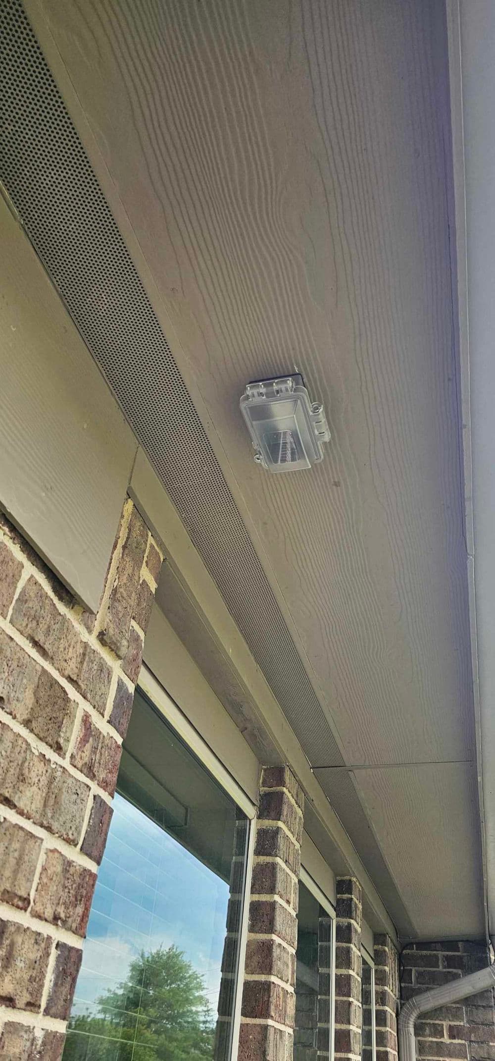 Clear outdoor light fixture mounted under eaves of a brick home, enhancing exterior illumination.